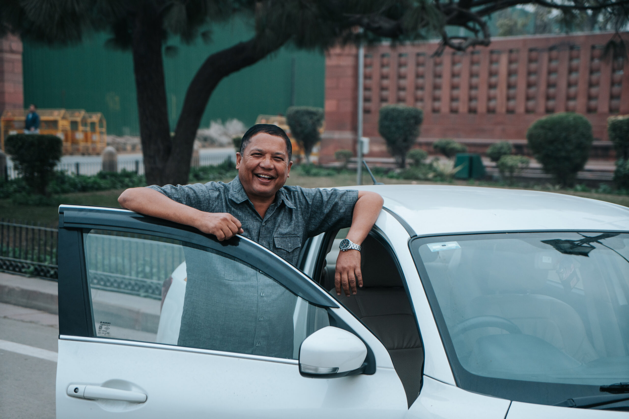 A Private Driver Beside His Car in India Smiling private driver standing by the open door of his white car near a red sandstone monument in India