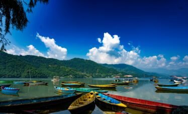Colorful wooden boats on Phewa Lake in Pokhara, Nepal, with World Peace Pagoda on the hilltop