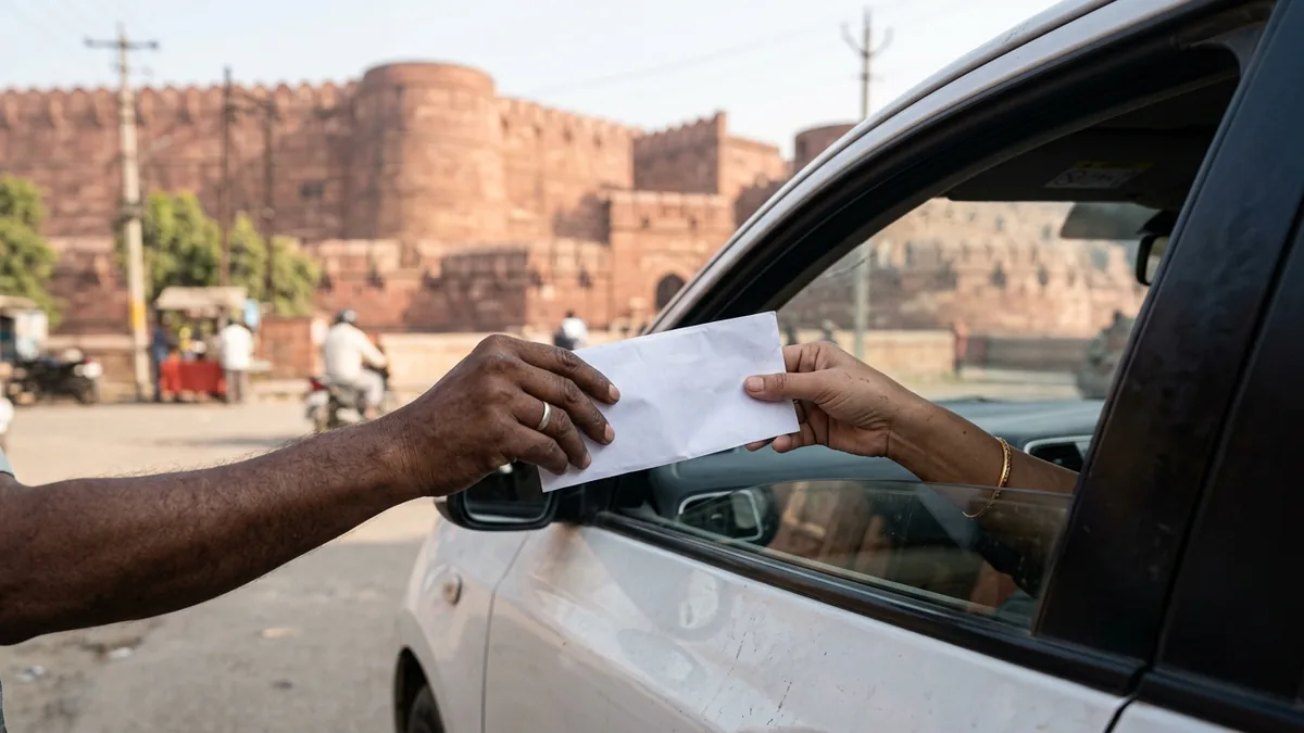Hand passing a white envelope to a driver through a car window in India