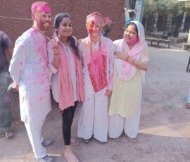 Celebrating Holi the authentic way—with a local Indian family in their hometown. Western tourists wearing traditional white kurtas covered in pink Holi colors celebrating with local Indian family