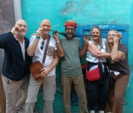 Our travelers sharing a fun moment with a local Rajasthani man during their Jodhpur tour. Happy tourists posing with traditional Rajasthani man with long mustache and turban in blue city Jodhpur, India